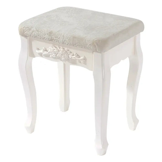 Een witte, klassieke houten kruk met gedetailleerde bloemversiering en een zacht, crèmekleurig gestoffeerd zitvlak. Perfect voor een elegante make-up of schoenenstijl in een slaapkamer of badkamer.