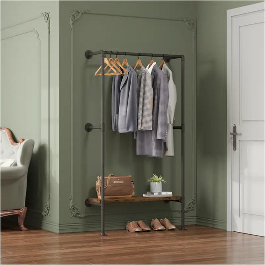 Een industriële kledingrek met donkergrijze metalen constructie en houten hangers, beladen met grijze jassen en een geruite trui, staat in een stijlvolle kamer. Onder het rek staat een houten plank met een bruine tas, een plant en schoenen, ideaal voor een moderne kledingopslag.