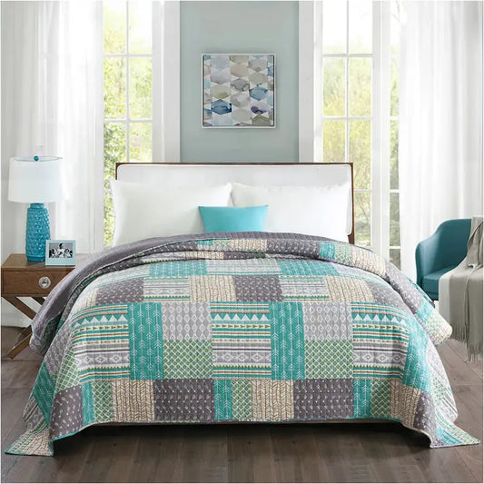 Een patchwork deken in turquoise, grijs en beige met geometrische patronen, op een bed met witte kussens. Perfect voor een moderne slaapkamerdecoratie met een bohemian flair.
