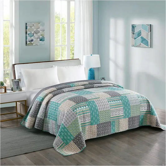 Een patchwork deken in turquoise, grijs en beige met geometrische patronen, op een bed met witte kussens en een blauwe accentkussen. Ideaal voor een moderne slaapkamerdecoratie met een bohemian flair.
