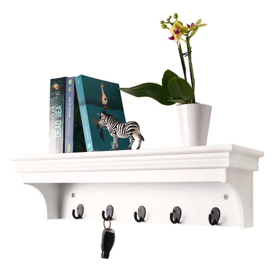 Een witte wandplank met vijf zwarte haakjes, waarvan één een sleutel draagt, en een boek met een zebra op de omslag. Perfect voor huiselijke decoratie en praktische opbergruimte in de hal of woonkamer.