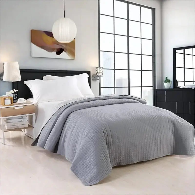 Grijs, gestikt dekbed met ruitpatroon op een modern bed in een minimalistische slaapkamer, compleet met witte kussens en een houten nachtkastje. Ideaal voor comfort en stijl in een moderne slaapkamer.