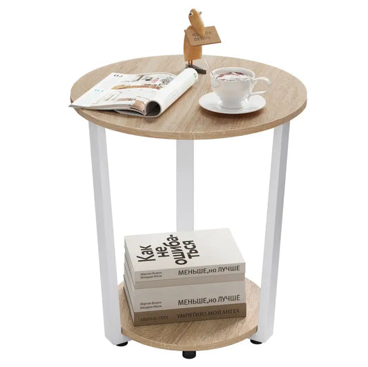 Een ronde bijzettafel met licht houten blad en witte metalen poten, voorzien van een ondersteunende plank. Ideaal voor woonkamer of slaapkamer als extra opslagruimte.