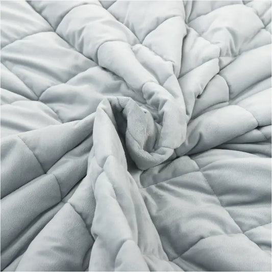 Lichtgrijze, gestikte deken met ruitpatroon op een modern bed in een minimalistische slaapkamer. Geïntegreerd in een rustige slaapomgeving met houten accenten en hangende lampen.