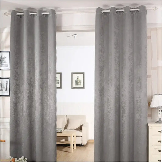 Grijze, textuurrijke gordijnen met oogjes hangen elegant voor een woonkamer, waarbij een lichtbeige bank en houten meubels zichtbaar zijn. Perfect voor moderne interieurs en zonlichtregulering.