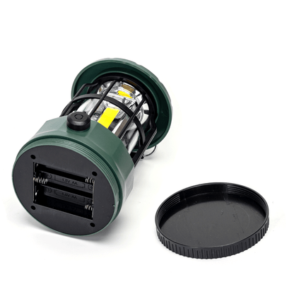 Groene, waterdichte kamplamp met zwart metaalframe en helder glas, uitgerust met USB-poorten en een opvallende gele LED. Perfect voor avonturen, kamperen en nachtelijke wandelingen in de natuur.