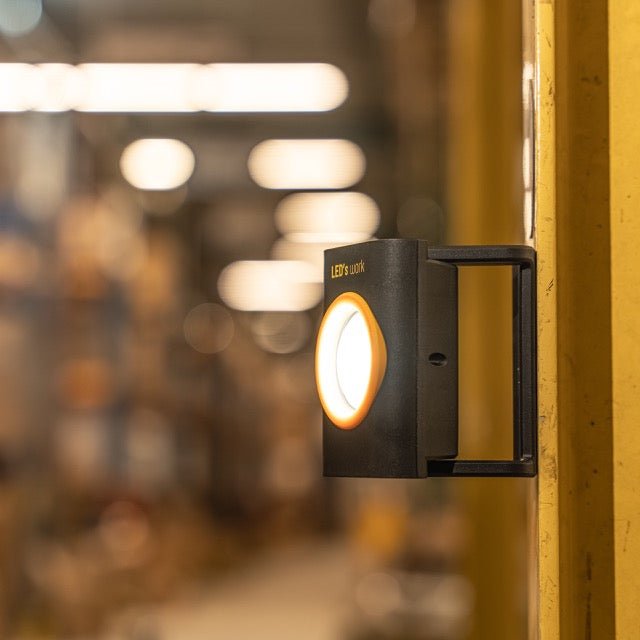 Zwart LED-lampje met geel kader en magnetische aansluiting, voor gebruik in werkomgevingen. Geen batterij nodig, geschikt voor reparaties en onderhoud.