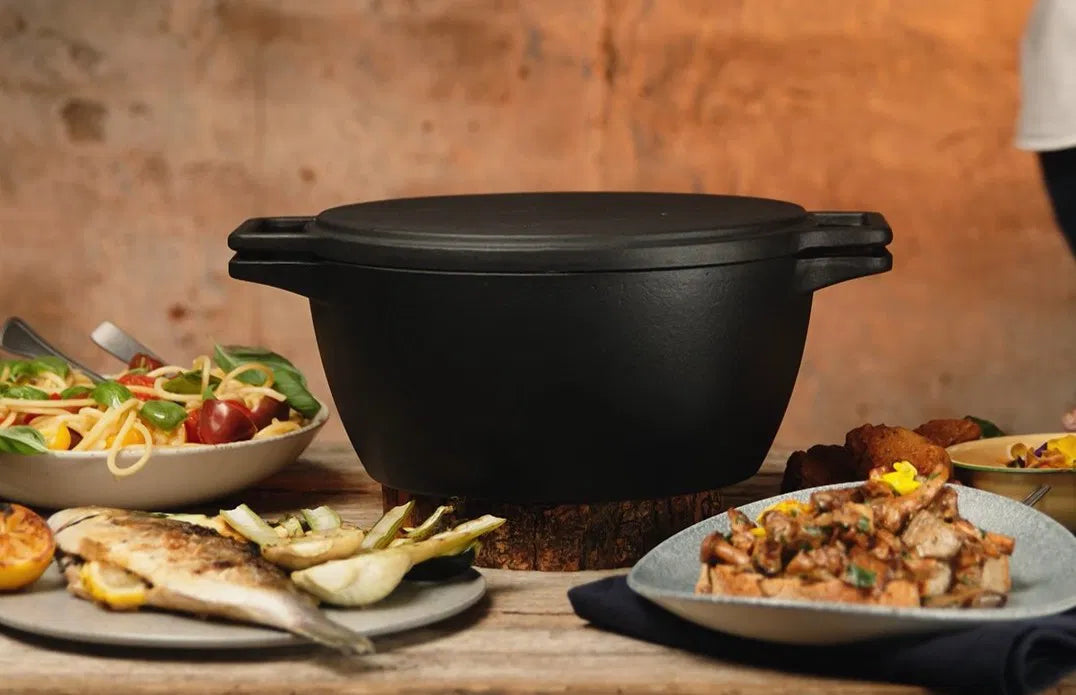 Zwarte kookpan van gietijzer met afsluitende deksel en stevige handvatten, geschikt voor grillen en koken op open vuur. Robuust ontwerp voor outdoor kookplekken en barbecue-avonden.