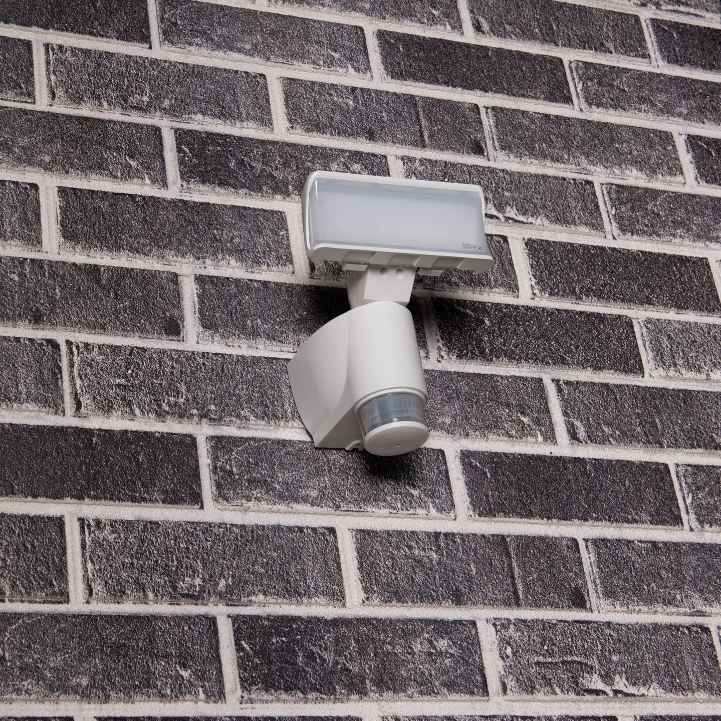 Een witte bewegingssensorlamp met transparante kap, geschikt voor buitenverlichting. Het apparaat detecteert beweging en is ideaal voor veilige verlichting van tuinen en gangpaden.