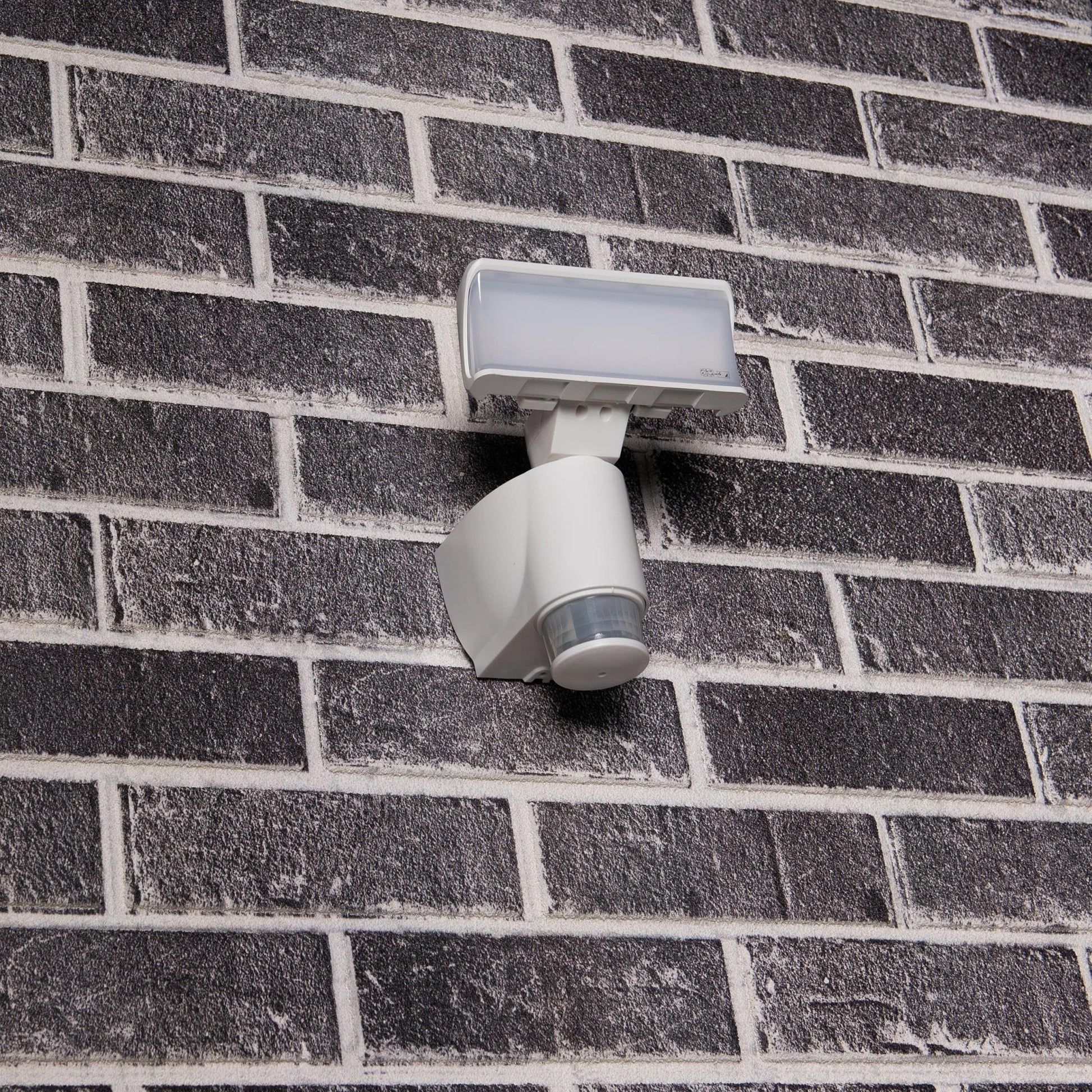 Een witte bewegingssensorlamp met transparante kap, geschikt voor buitenverlichting. Het apparaat detecteert beweging en is ideaal voor veilige verlichting van tuinen en gangpaden.