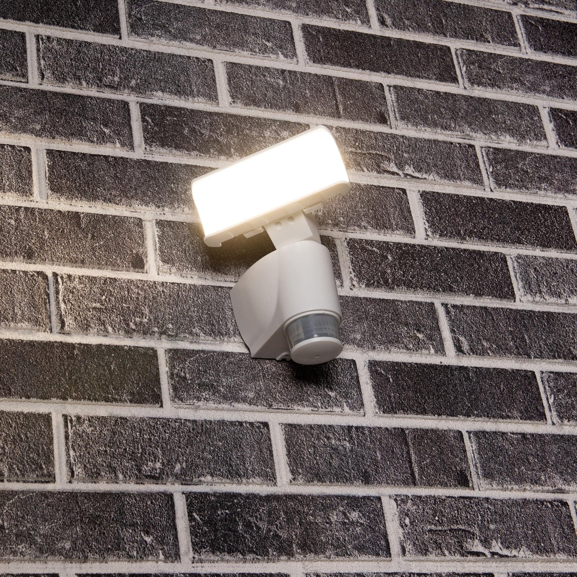 Een witte bewegingssensorlamp met transparante kap en sensorkop, ontworpen voor buitenverlichting. Geïntegreerd bewegingssensor detecteert beweging voor automatische verlichting.