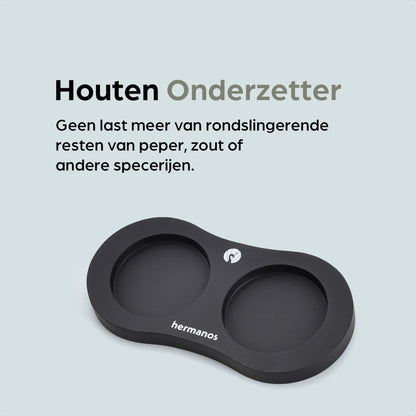 Een witte en zwarte houten pepermolen met goudkleurige doppen, geplaatst op een zwarte standaard met het merk 'hermanos'. Inclusief extra zilveren doppen voor keuken- en eetkamergebruik.
