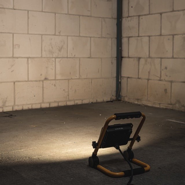 Een robuuste, gele en zwarte LED werklamp met verstelbare voeten en handgreep, geschikt voor bouw- en reparatiewerkzaamheden. Zichtbare LED-panelen en sterk ontworpen frame voor betrouwbare verlichting.