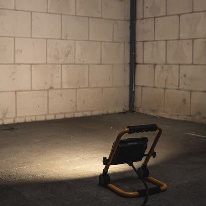Een robuuste, gele en zwarte LED werklamp met verstelbare voeten en handgreep, geschikt voor bouw- en reparatiewerkzaamheden. Zichtbare LED-panelen en sterk ontworpen frame voor betrouwbare verlichting.