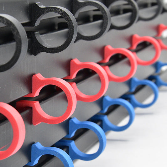 Rode, blauwe en zwarte plastic klemmen voor fietsen, geplaatst op een donkergrijze metalen rail. Geschikt voor fietsen en andere sporttoepassingen, met een heldere kleurcontrast en robuust materiaal.