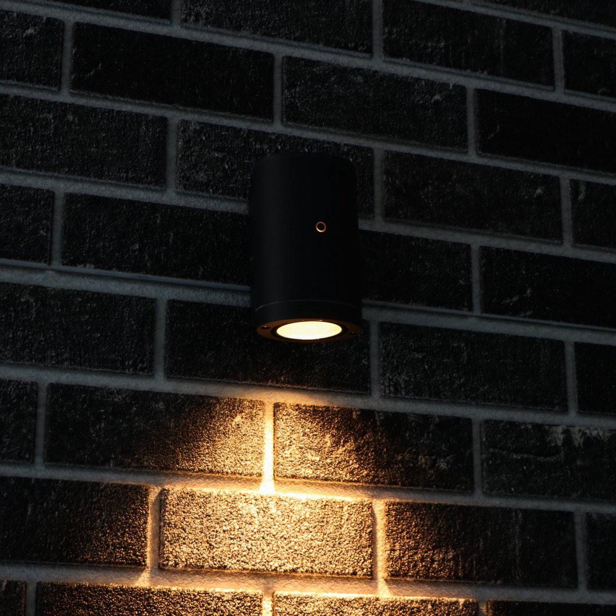 Zwart, cilindrisch wandlamp met goudkleurige rand en warm wit licht, geschikt voor moderne interieurs. Ideaal voor accentverlichting in woon- en werkkamers.