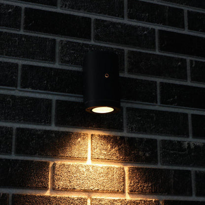 Zwart, cilindrisch wandlamp met goudkleurige rand en warm wit licht, geschikt voor moderne interieurs. Ideaal voor accentverlichting in woon- en werkkamers.
