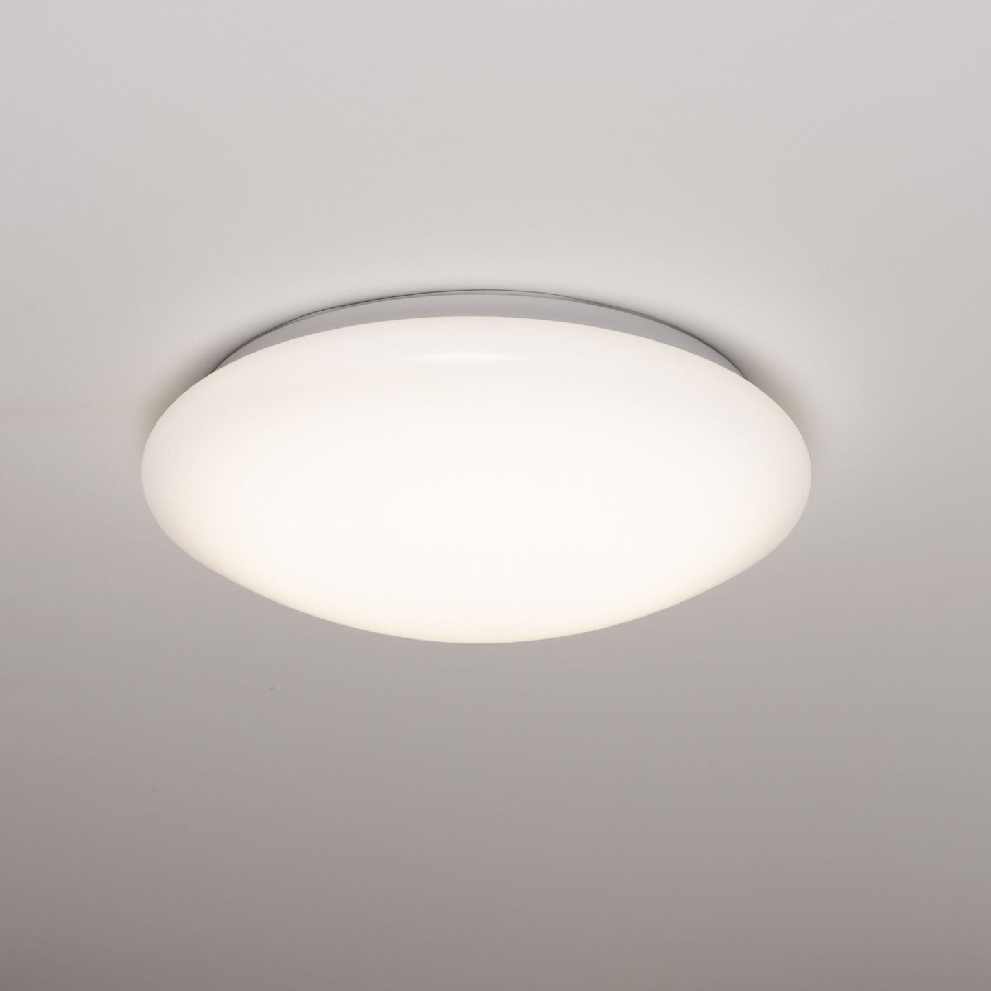 Een witte, ronde plafondlamp met een gladde, mat-witte diffuser en een zilverkleurige rand. Geschikt voor moderne interieurs en als energiezuinige verlichting in woon- en werkkamers.