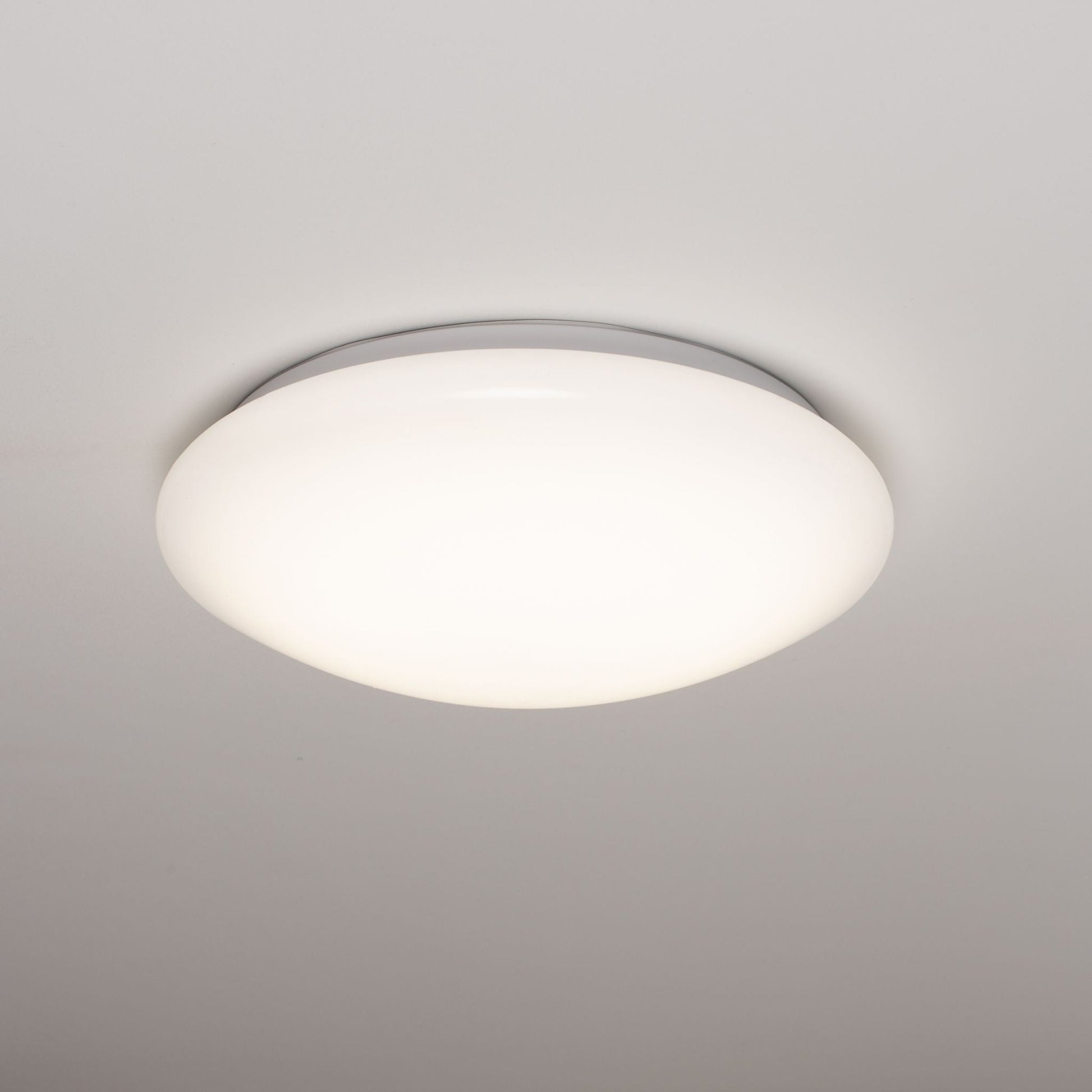 Een witte, ronde plafondlamp met een gladde, mat-witte diffuser en een zilverkleurige rand. Geschikt voor moderne interieurs en als energiezuinige verlichting in woon- en werkkamers.
