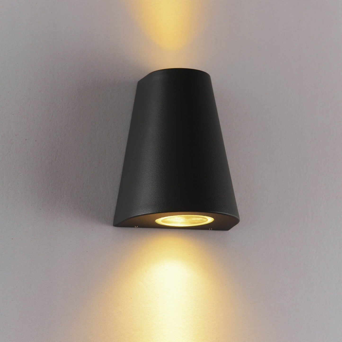 Zwart, cilindrisch wandlampje met warm wit licht, bevestigd aan een textuurrijke betonmuur. Perfect voor moderne buitenverlichting en architectonische accentverlichting.