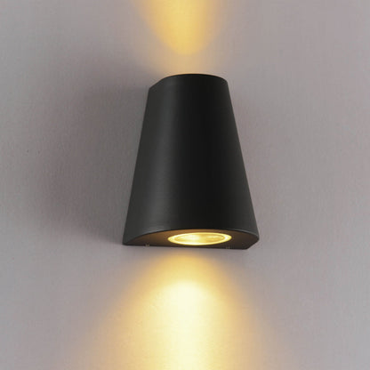 Zwart, cilindrisch wandlampje met warm wit licht, bevestigd aan een textuurrijke betonmuur. Perfect voor moderne buitenverlichting en architectonische accentverlichting.