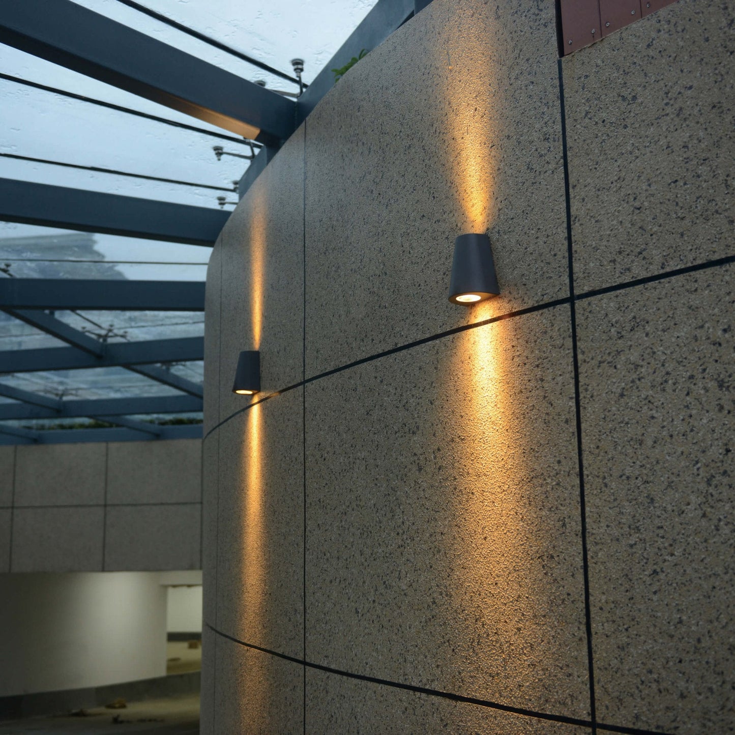 Zwart, cilindrisch wandlampje met warm wit licht, bevestigd aan een textuurrijke betonmuur. Ideaal voor moderne buitenverlichting en architectonische accentverlichting.