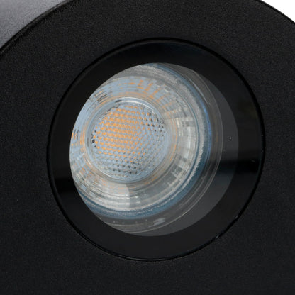 Zwart, cilindrisch wandlampje met warm wit licht, bevestigd aan een textuurrijke betonmuur. Perfect voor moderne buitenverlichting en architectonische accentverlichting.