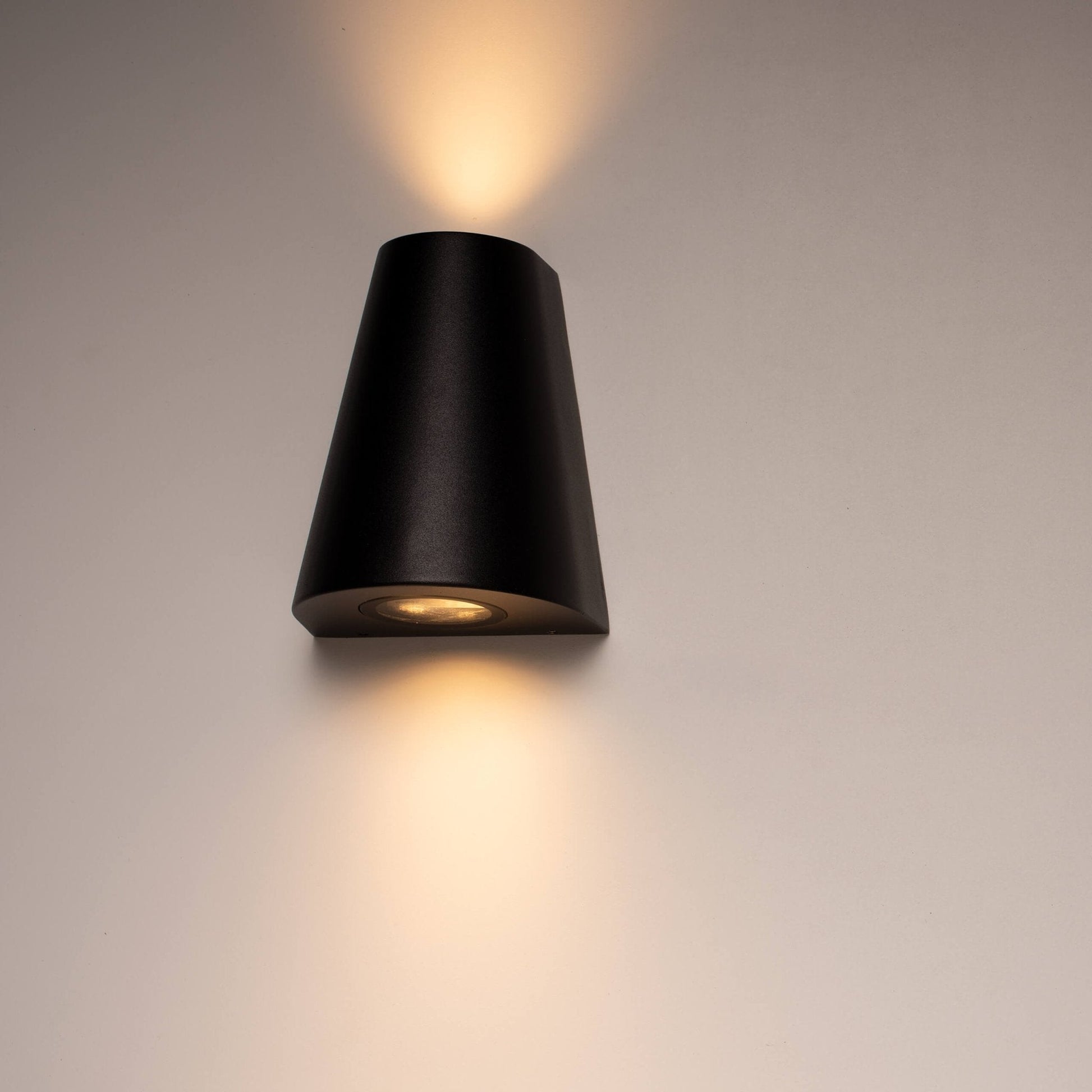 Zwart, cilindrisch wandlampje met warm wit licht, bevestigd aan een textuurrijke betonmuur. Ideaal voor moderne buitenverlichting en architectonische accentverlichting.