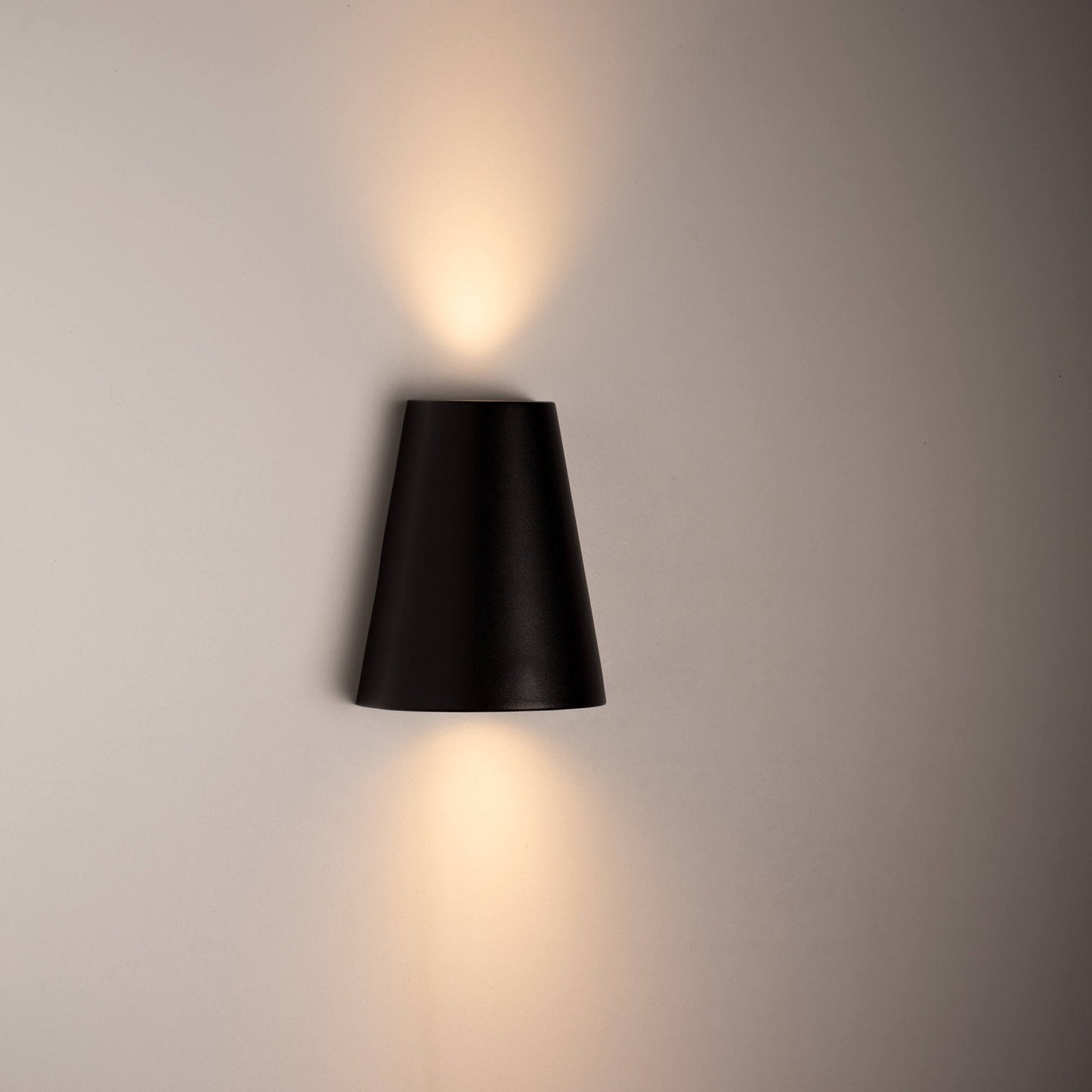 Zwart, cilindrisch wandlampje met warm wit licht, bevestigd aan een textuurrijke betonmuur. Perfect voor moderne buitenverlichting en architectonische accentverlichting.