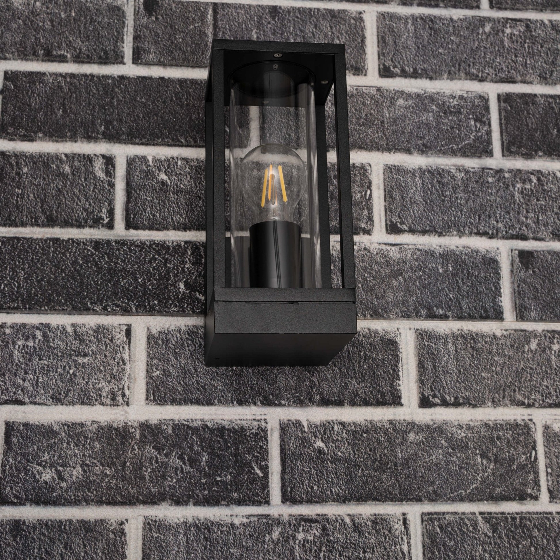 Een zwart, rechthoekig buitenspot met glazen panelen en een gloeiende filamentlamp. Perfect voor warme verlichting op terrassen of in de tuin.