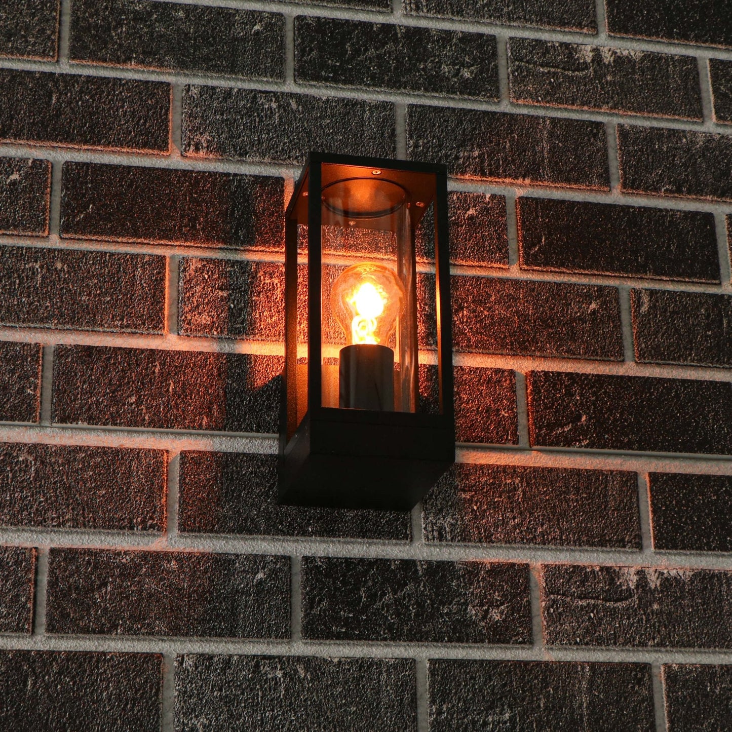 Een zwart, rechthoekig buitenspot met glazen panelen en een gloeiende vintage lamp. Perfect voor warme verlichting op terras of veranda.