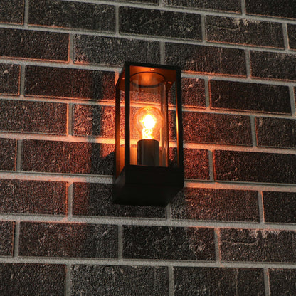 Een zwart, rechthoekig buitenspot met glazen panelen en een gloeiende vintage lamp. Perfect voor warme verlichting op terras of veranda.