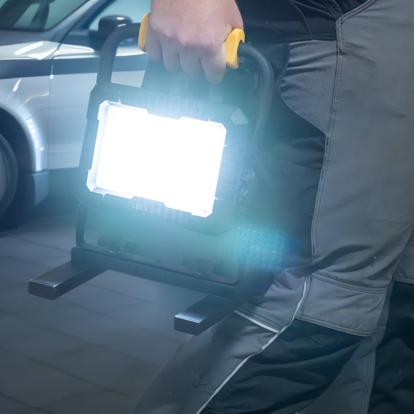 LED’s work werktuigverlichting met geïntegreerde gele handgreep en vier zwarte adapteren voor Bosch, Einhell, Makita en Metabo, geschikt voor professionele werkomgevingen en werkplaatsverlichting.