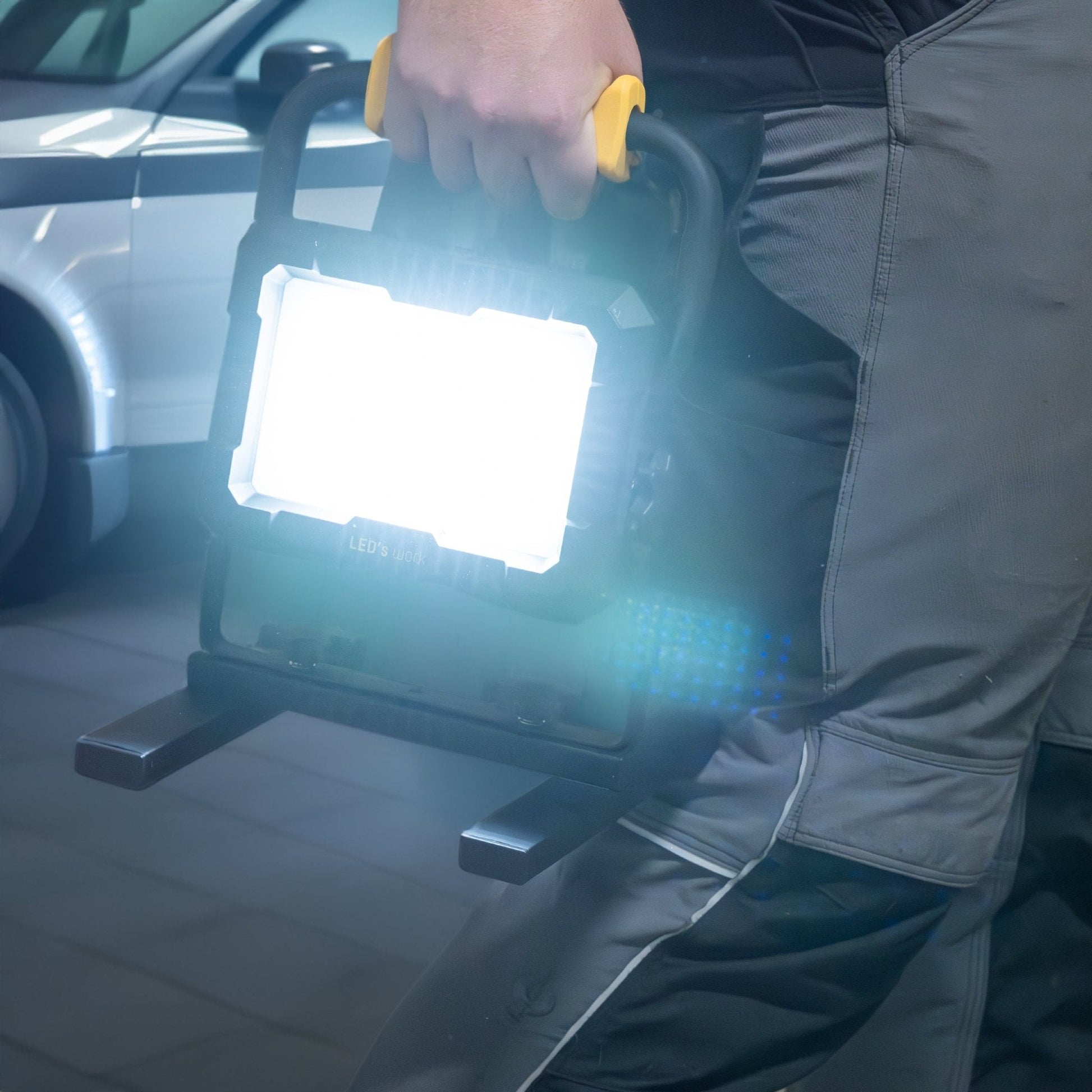LED’s work werktuigverlichting met geïntegreerde gele handgreep en vier zwarte adapteren voor Bosch, Einhell, Makita en Metabo, geschikt voor professionele werkomgevingen en werkplaatsverlichting.