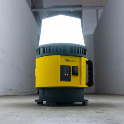Een gele en zwarte batterijoplaadbare werklamp met witte kap en rode accu-connector, geschikt voor industriële of bouwtoepassingen. Geen accu meegeleverd.