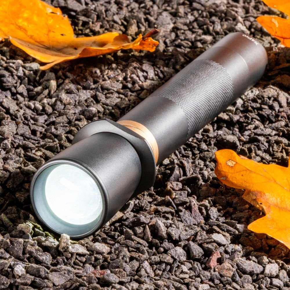Zwarte, matte zaklamp met textuurde grip en zichtbare focusring, geschikt voor avondwandelingen en nachtverlichting. Robuust ontwerp met goudkleurige accenten voor betere grip en stijl.