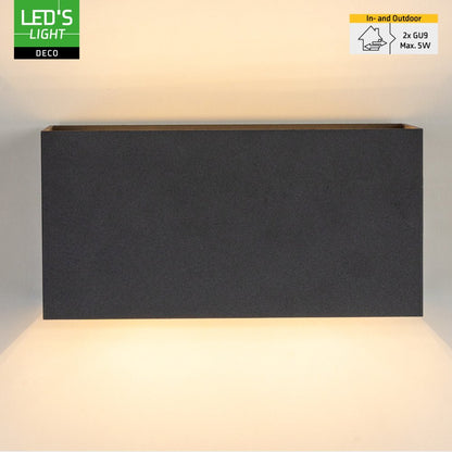 Een moderne, zwarte wandlamp met warm wit licht, bevestigd aan een bakstenen muur. Ideaal voor buitenverlichting en moderne tuin- of terrasdecoratie.