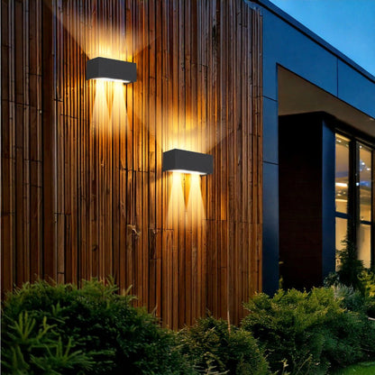 Een moderne, zwarte wandlamp met warm wit licht, bevestigd aan een bakstenen muur. Ideaal voor buitenverlichting en moderne tuin- of terrasdecoratie.
