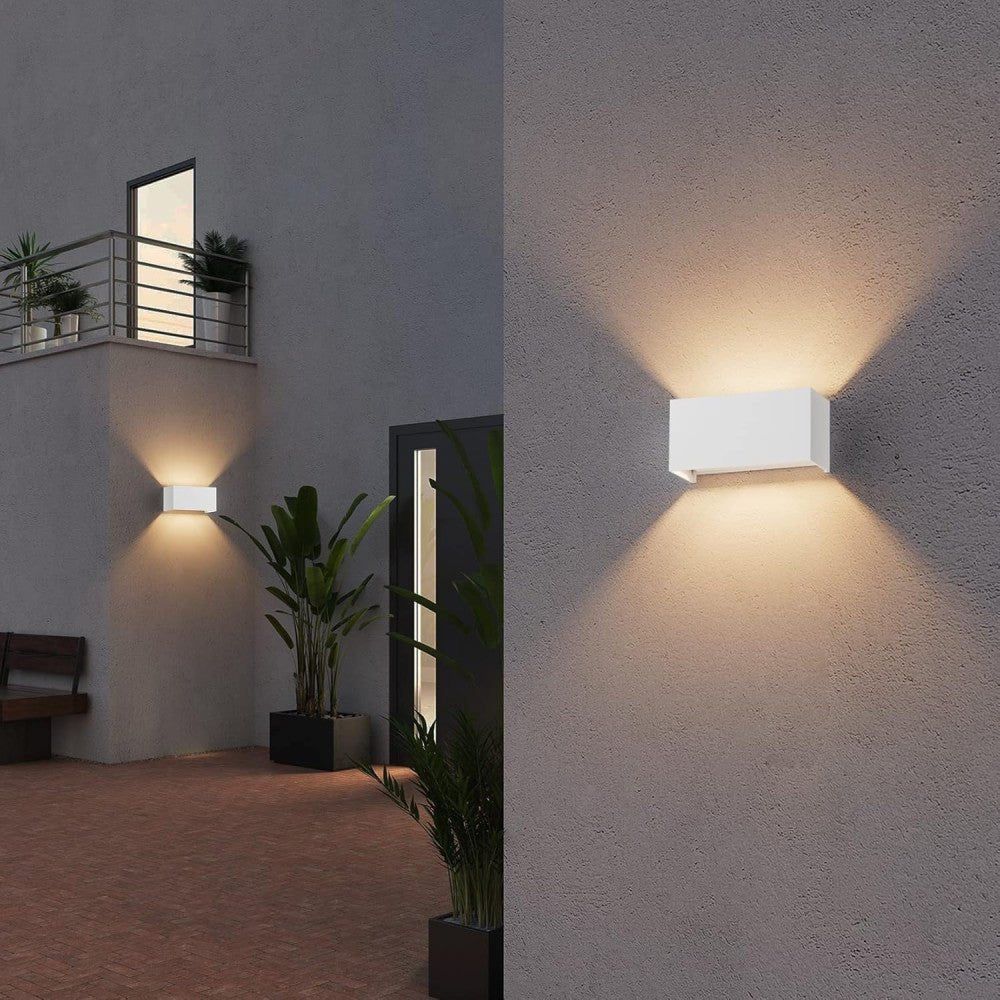 Een witte, rechthoekige wandlamp met warm wit licht, bevestigd aan een grijze bakstenen muur. Ideaal voor buitenverlichting en moderne tuin- of terrasdecoratie.