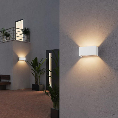 Een witte, rechthoekige wandlamp met warm wit licht, bevestigd aan een grijze bakstenen muur. Ideaal voor buitenverlichting en moderne tuin- of terrasdecoratie.