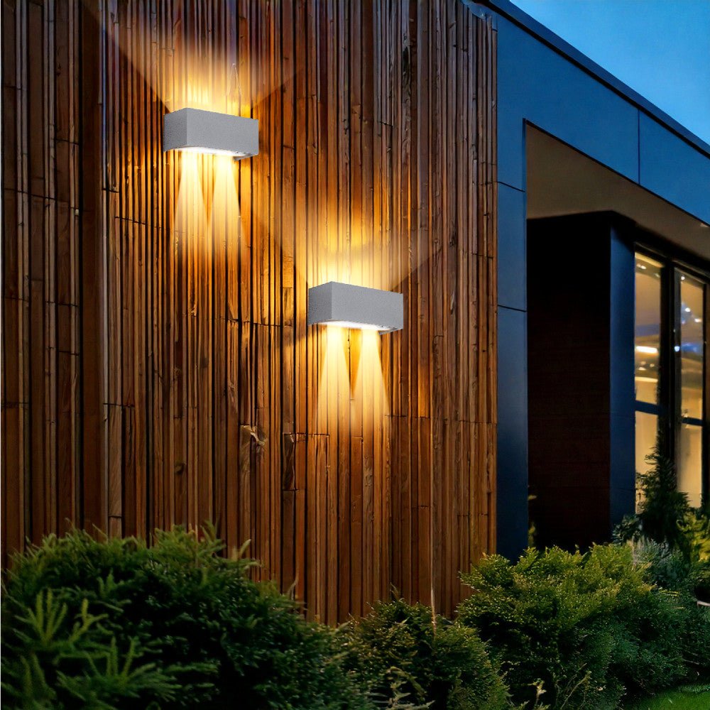 Een witte, rechthoekige wandlamp met zacht geel licht, bevestigd aan een grijze bakstenen muur. Perfect voor moderne buitenverlichting en nachtverlichting van terrassen of veranda’s.