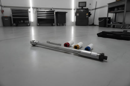 Zilverkleurige schroefspanner in zwarte houder, met kleurrijke (blauw, geel, rood) accessoires. Geschikt voor precisie- en reparatiewerkzaamheden in de auto- en houtbewerkingssector.
