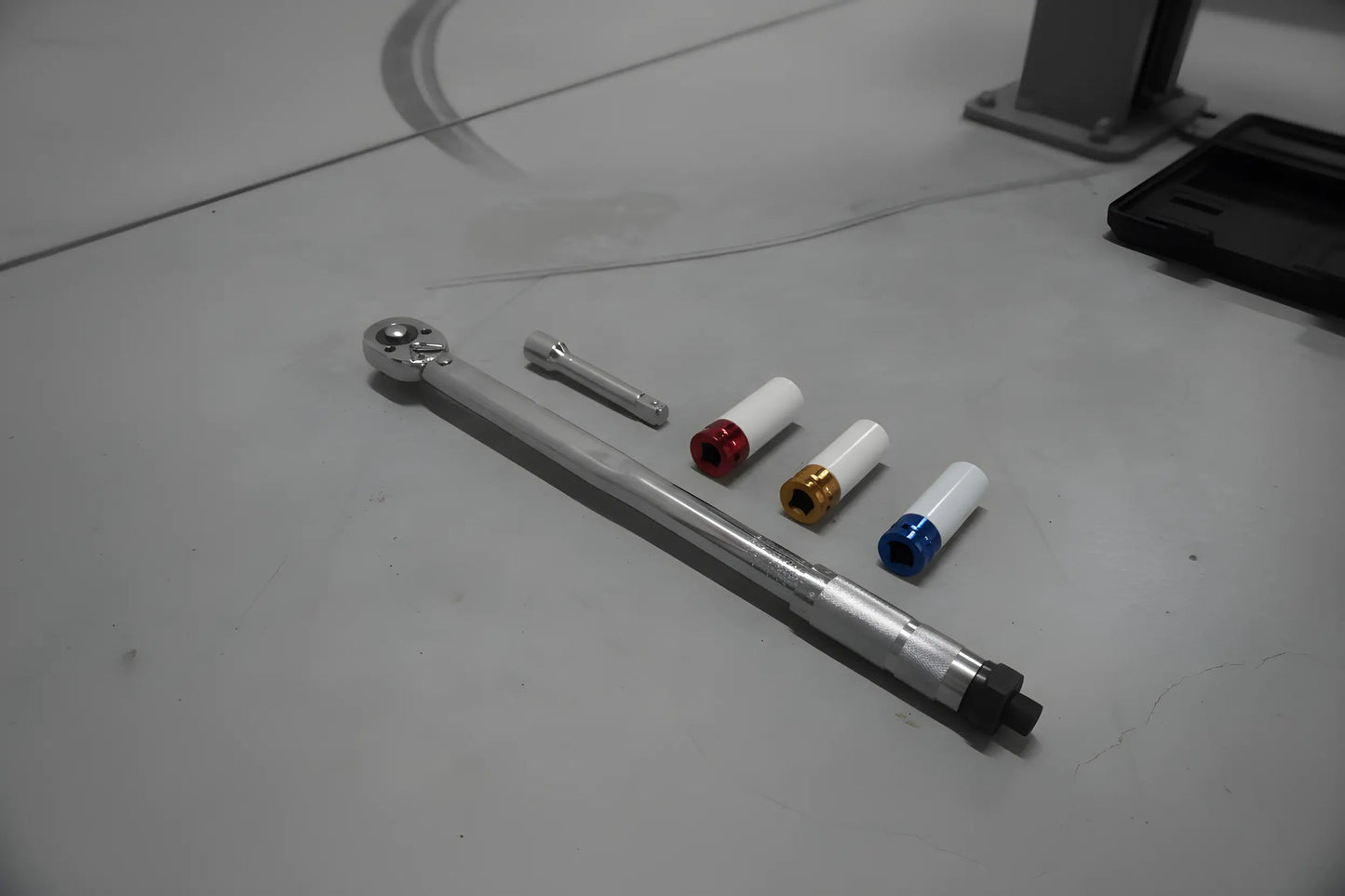 Zilverkleurige schroefspanner in zwarte houder, met kleurrijke (blauw, geel, rood) aanpasbare koppen. Geschikt voor precisie-schroefwerk in auto’s en machines.