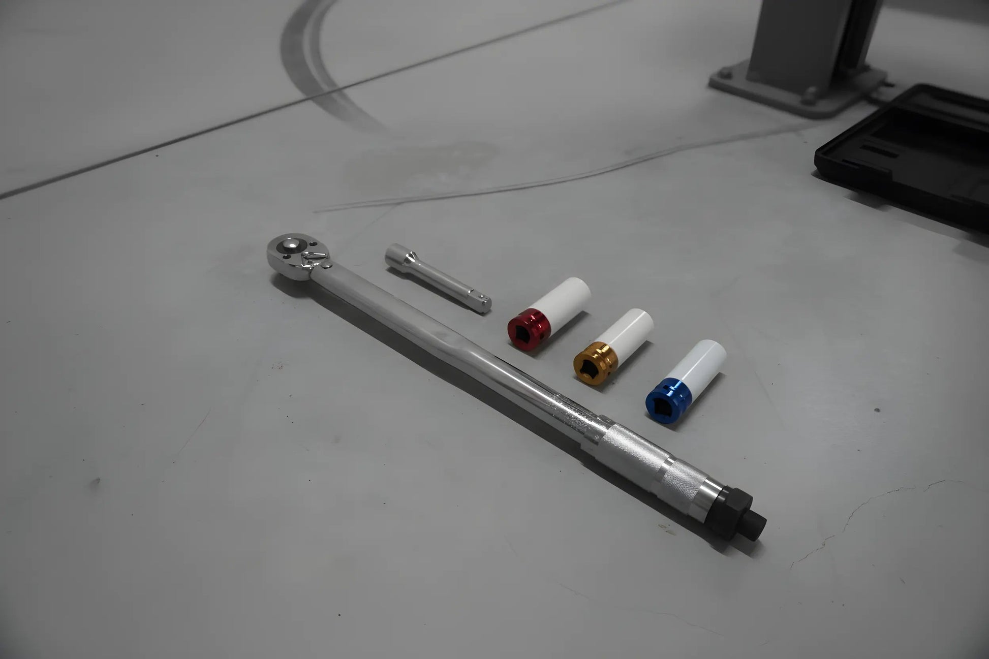 Zilverkleurige schroefspanner in zwarte houder, met kleurrijke (blauw, geel, rood) aanpasbare koppen. Geschikt voor precisie-schroefwerk in auto’s en machines.