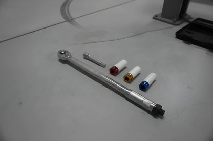 Zilverkleurige schroefspanner in zwarte houder, met kleurrijke (blauw, geel, rood) aanpasbare koppen. Geschikt voor precisie-schroefwerk in auto’s en machines.