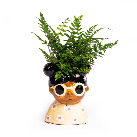 Een kleurrijke, keramische plantenpot in de vorm van een vrouw met zonnebril en bloemenjurk, gevuld met een groene varen. Perfect voor een stijlvolle, decoratieve binnenruimte of als unieke cadeau.