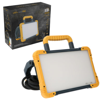 Een robuuste, gele en zwarte LED werklamp met handgreep en opgerolde kabel, geschikt voor professioneel gebruik in workshops of op bouwplaatsen.