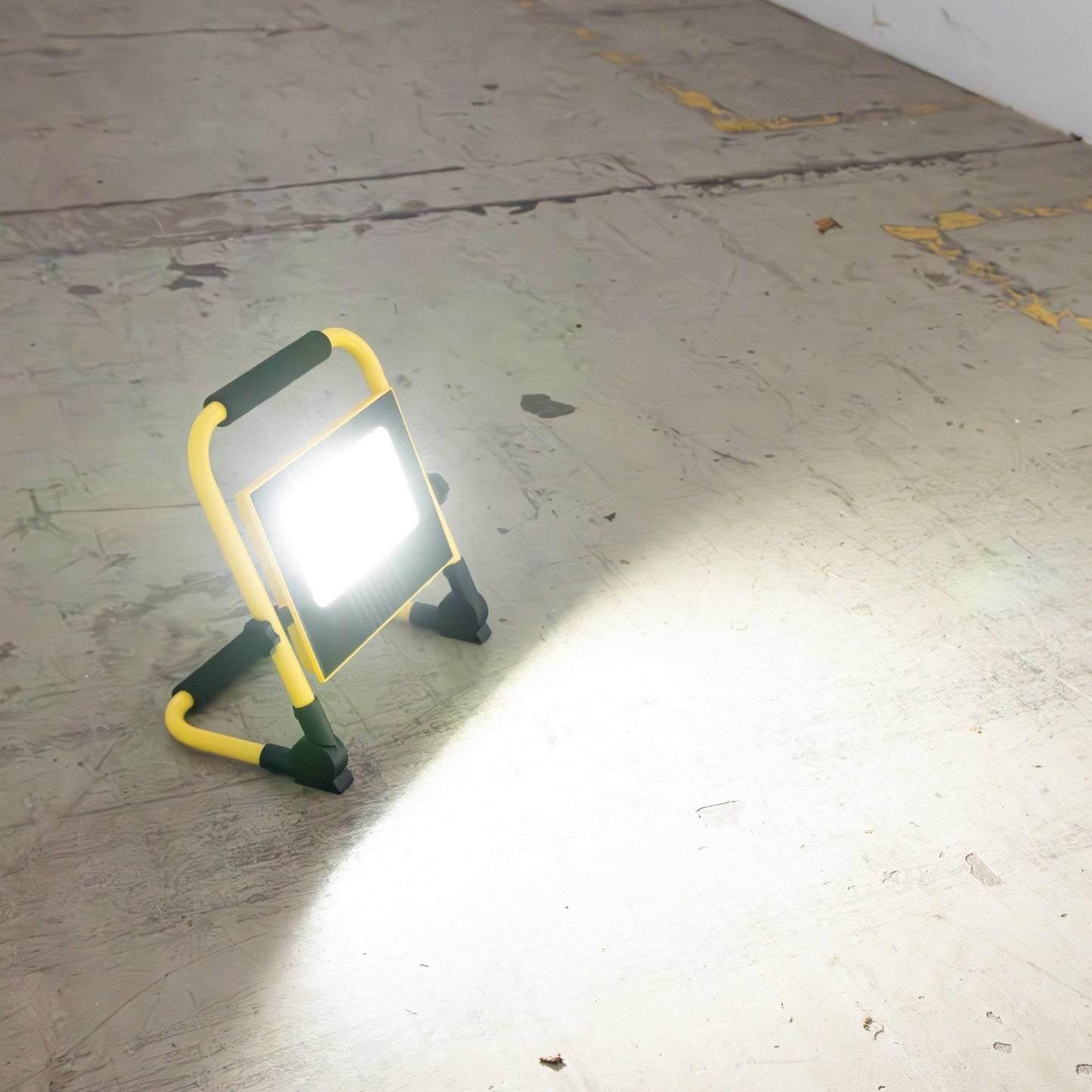 Geel opvouwbare LED werklamp met zwart handvat en verstelbare poten, geschikt voor bouw- en reparatiewerkzaamheden. Zichtbaar op de achtergrond: de verpakking met technische specificaties.