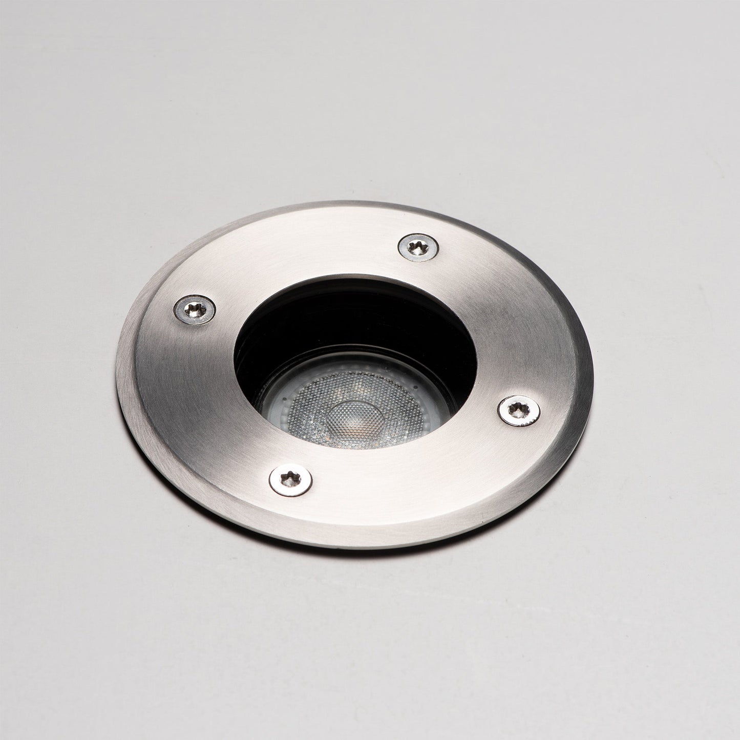 Zilverkleurige, ronde bodemlamp met glazen kap en zichtbare schroeven, voorzien van een zwarte cilindrische basis. Geschikt voor tuinverlichting en buitenverlichting.