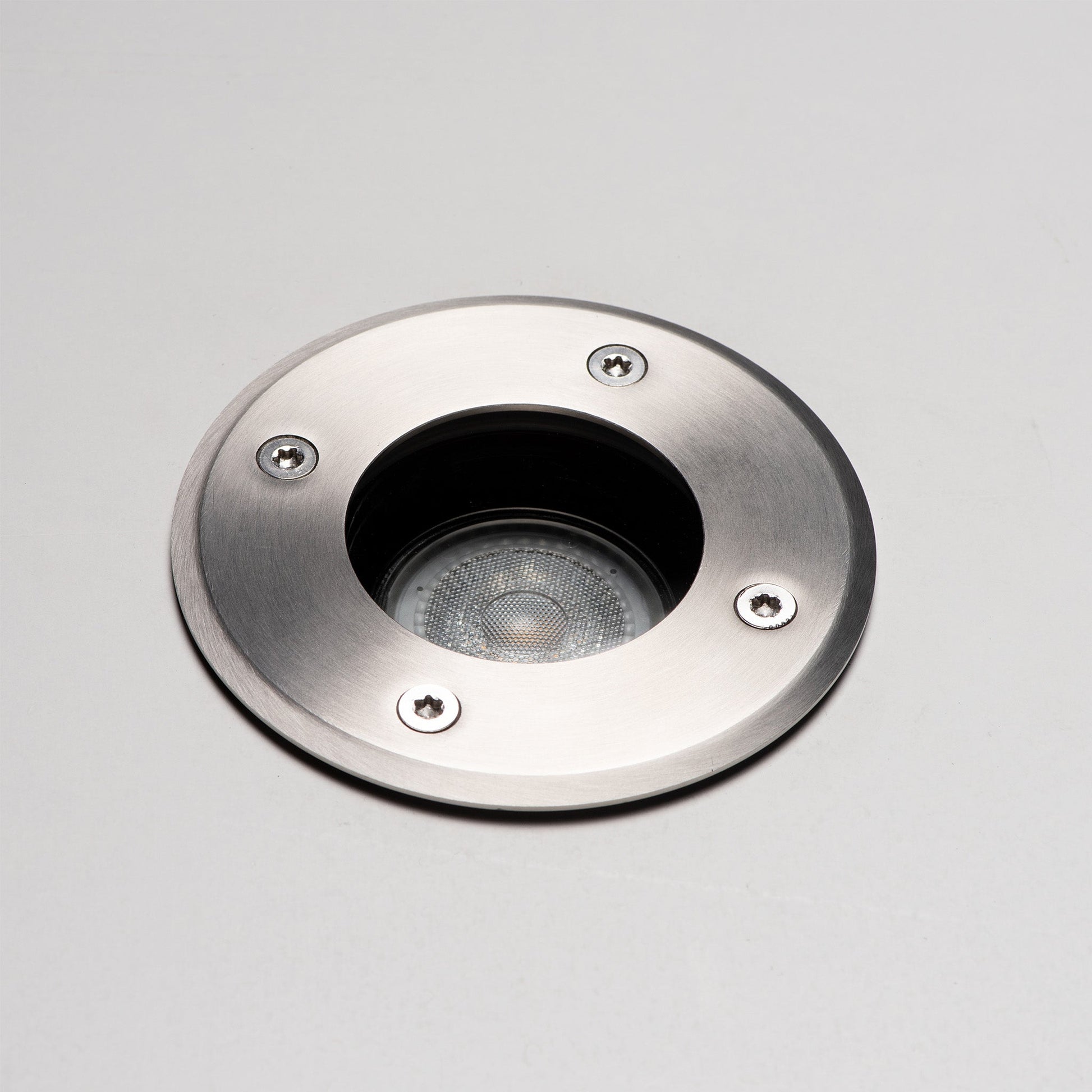 Zilverkleurige, ronde bodemlamp met glazen kap en zichtbare schroeven, voorzien van een zwarte cilindrische basis. Geschikt voor tuinverlichting en buitenverlichting.